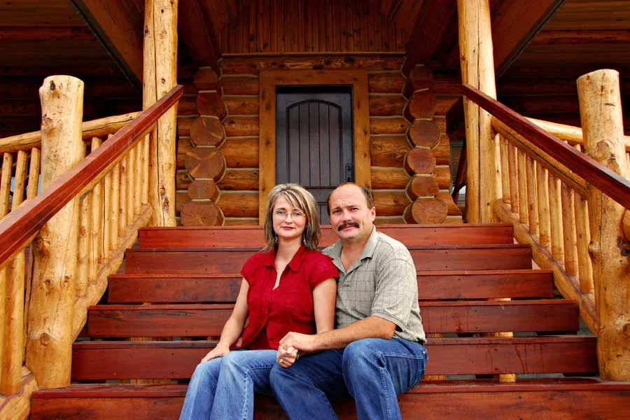 Jeff and Alana Lerwill sitting on the front steps of the log lodge they built