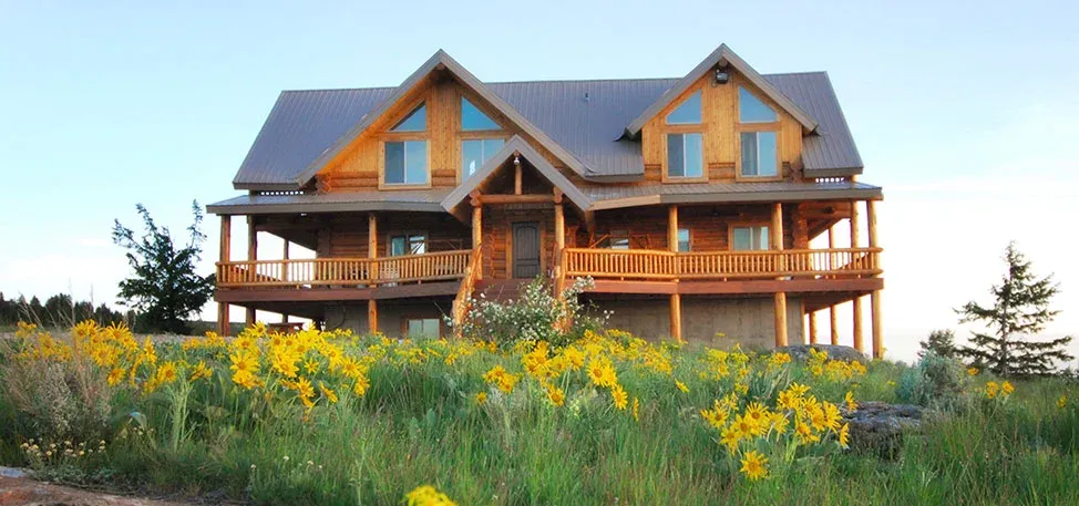 The log lodge at Rocky Mountain Elk Ranch above a hillside of yellow wildflowers