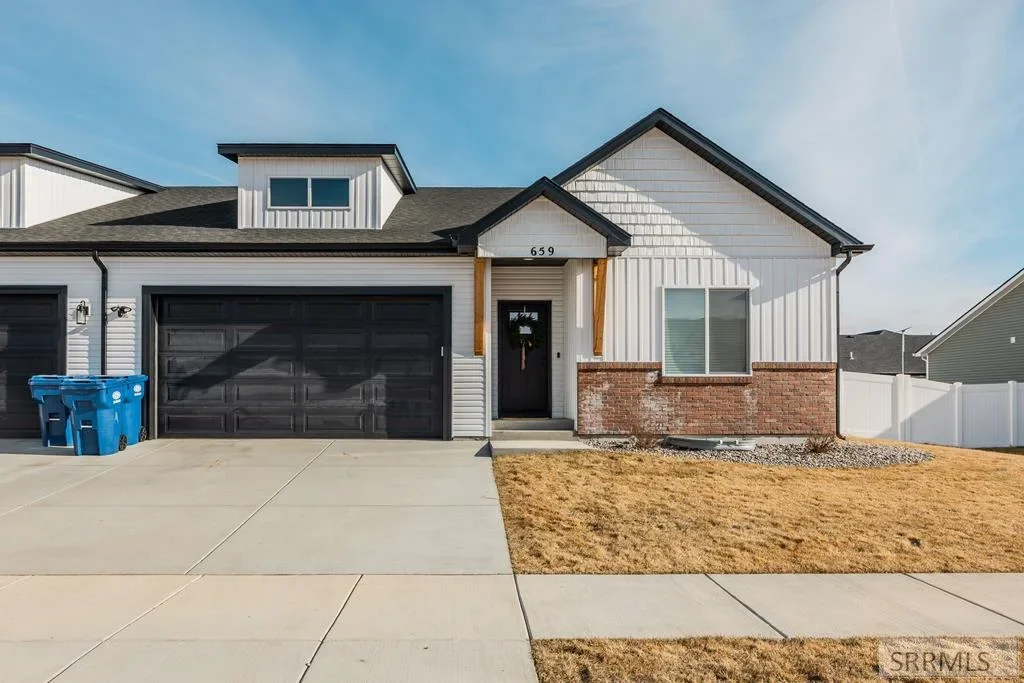 A new-construction home with white siding, brick accents, and a dark garage door in Sugar City