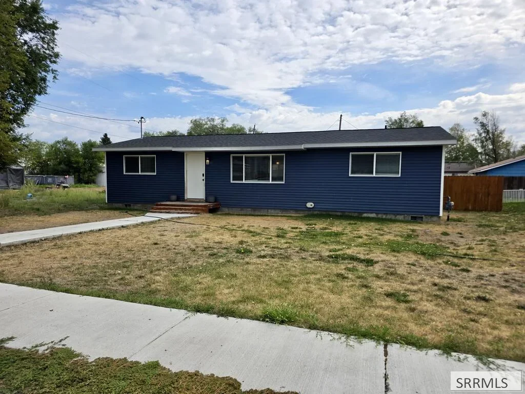 A single-level blue ranch home with a front lawn in St. Anthony, Idaho