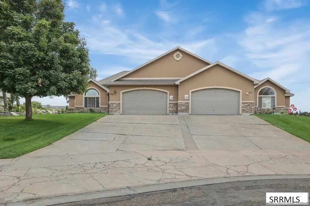 A stucco twin home with two garages, a wide driveway, and a green lawn in Rexburg